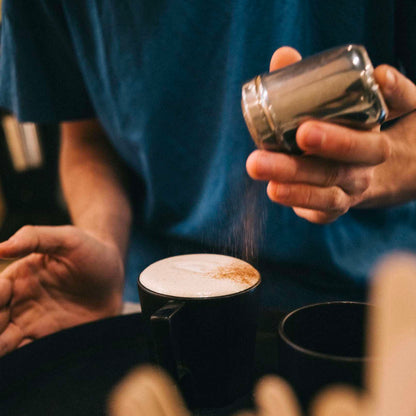 finition de la préparation du chai masala en saupoudrant un peu de cannelle par dessus la mousse