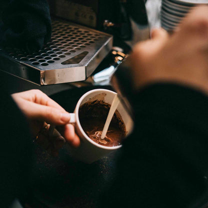photo du lait versé dans une tasse blanche dans un coffee shop pour finir la préparation du chocolat chaud by awachai