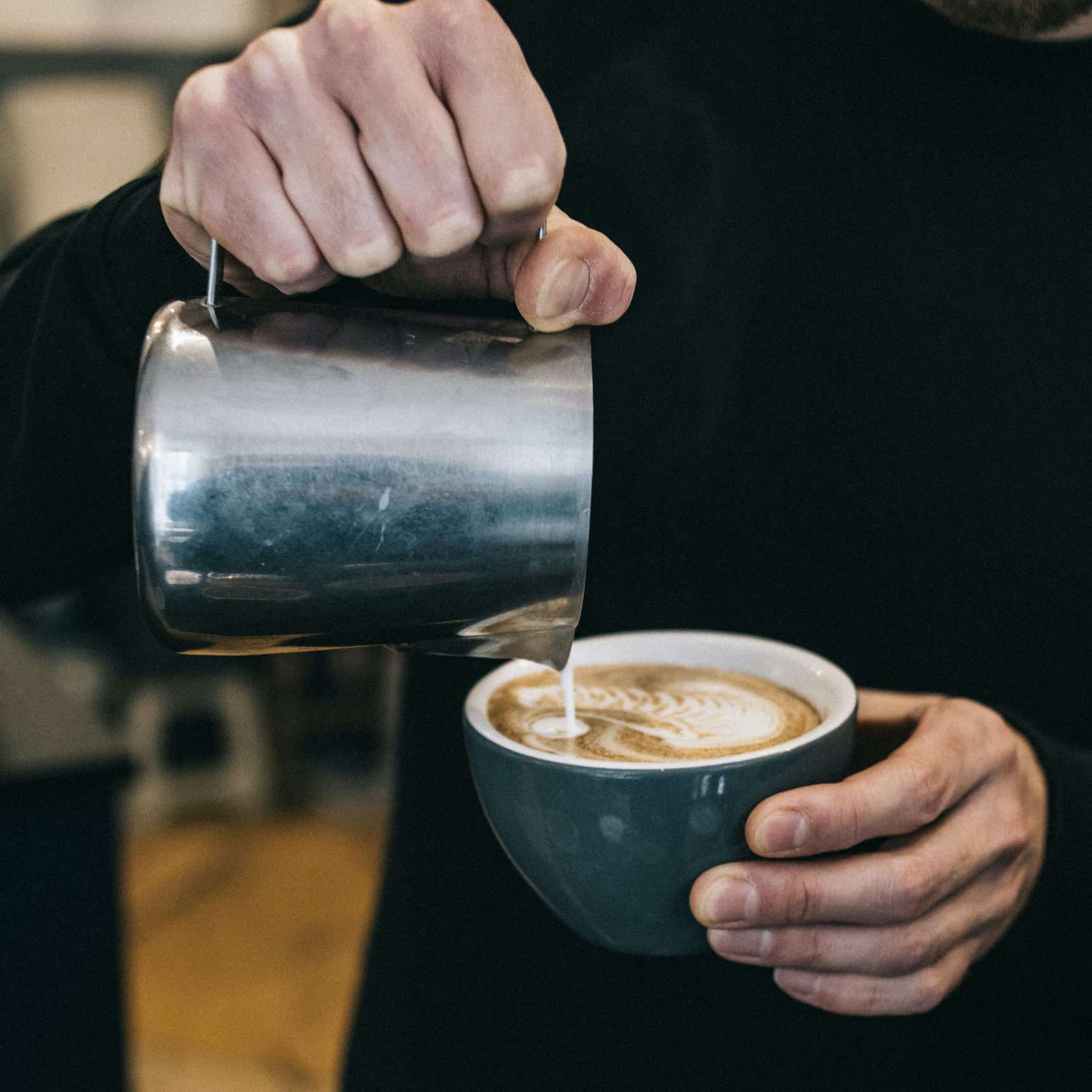 zoom sur les mains d'un barista qui termine la préparation d'un chai latte en ajoutant le lait