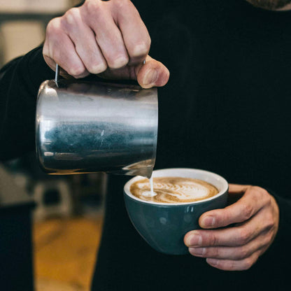 zoom sur les mains d'un barista qui termine la préparation d'un chai latte en ajoutant le lait